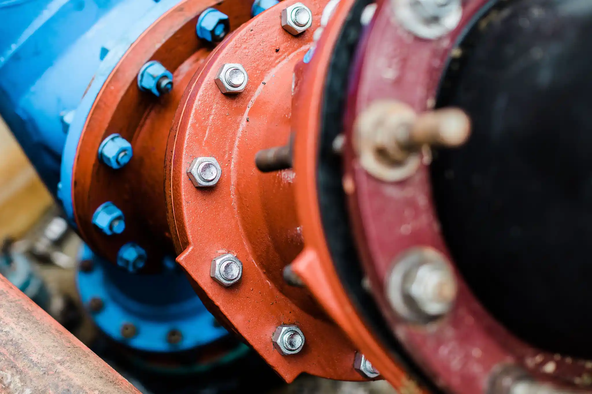 closeup of pipeline unions in multiple colors with new and old nuts and bolts holding them together.